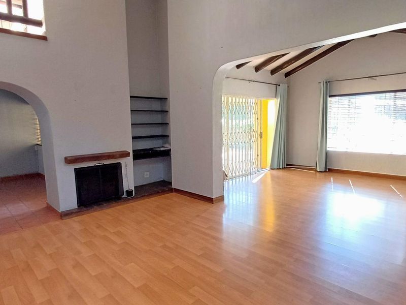 Spacious living area featuring laminate flooring, a built-in fireplace, exposed timber ceiling beams, and direct access to the outdoor area through a security gate.