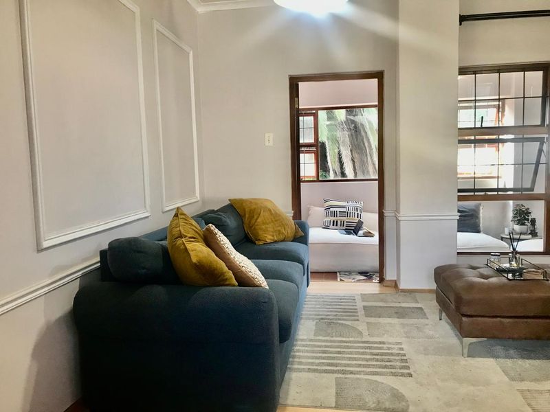 A cozy living room featuring decorative wall moulding, wainscoting, and timber-framed windows that allow natural light to flow through to the adjacent space.