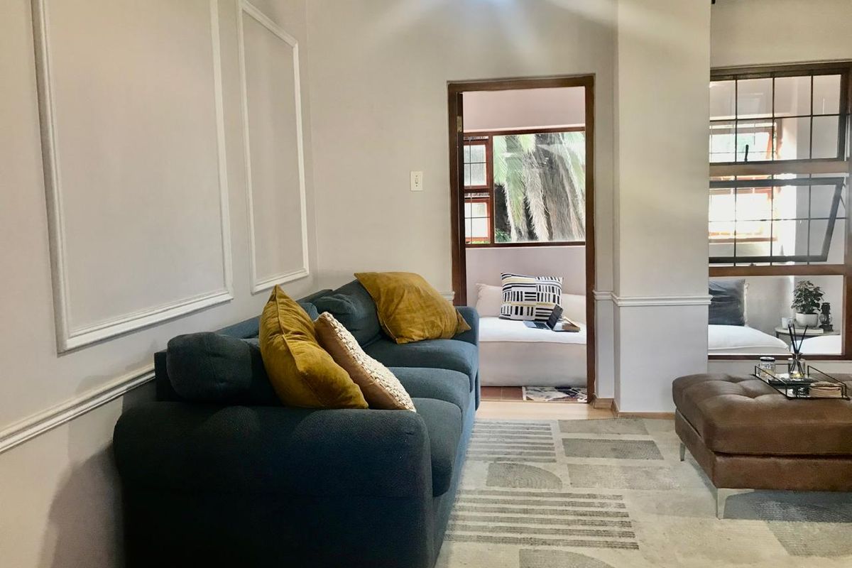 A cozy living room featuring decorative wall moulding, wainscoting, and timber-framed windows that allow natural light to flow through to the adjacent space.