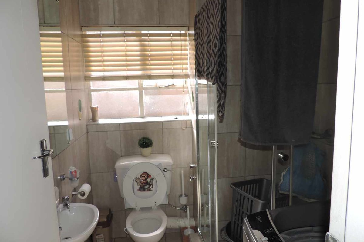 Compact bathroom featuring tiled walls, a pedestal basin, a toilet, and a glass-enclosed shower area with integrated laundry space.