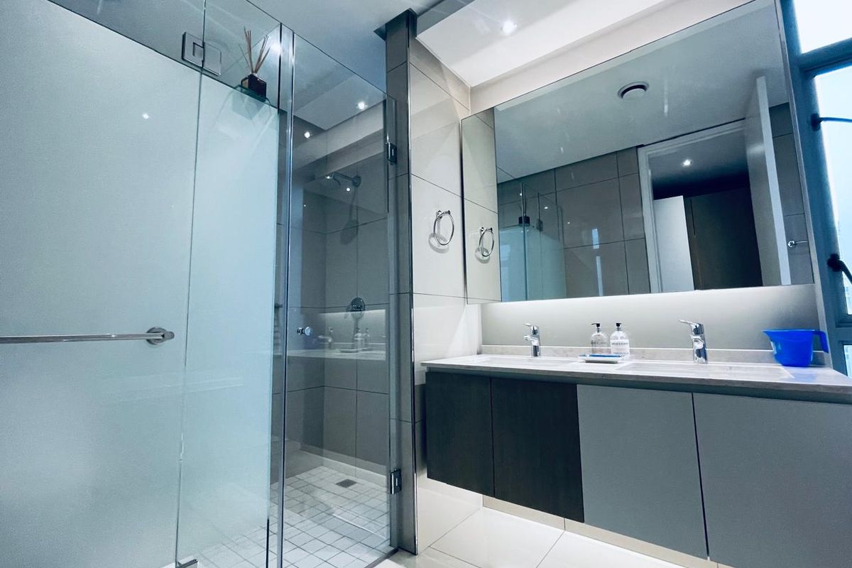 Modern bathroom featuring a double vanity with wall-mounted cabinetry, a large mirror, and a spacious glass-enclosed shower with contemporary tiling.