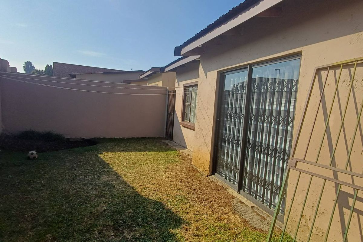 A private rear garden area featuring a small lawn, perimeter boundary wall, and sliding glass door access with security gate.