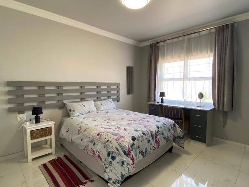 A well-maintained bedroom featuring tiled flooring, crown molding, and a built-in desk area with natural light.