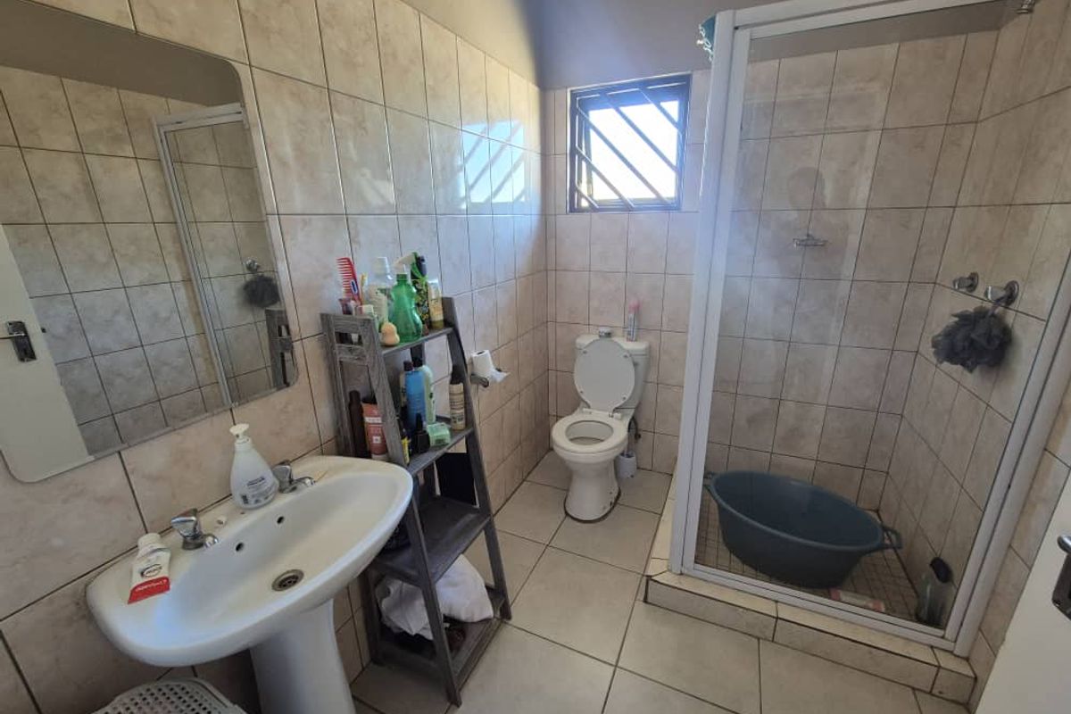 A functional bathroom featuring a pedestal basin, a shower enclosure, and a toilet, finished with neutral wall and floor tiling.