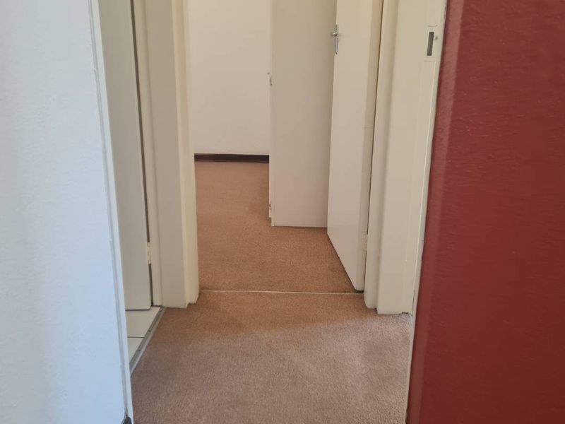 A narrow residential hallway featuring carpeted flooring and multiple internal doors, showing signs of wear and requiring cosmetic updates.