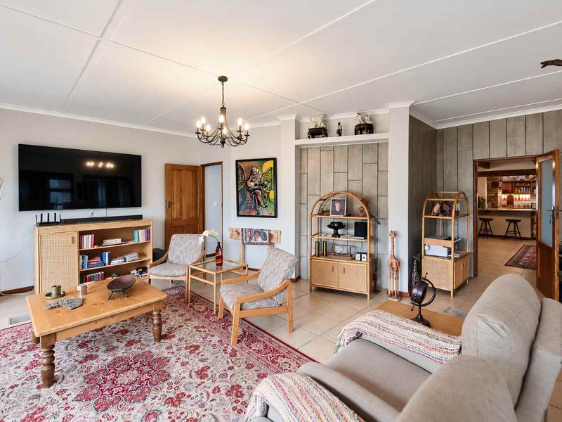 Spacious living room featuring tiled flooring, a decorative feature wall, and a classic chandelier, offering a comfortable and inviting atmosphere.