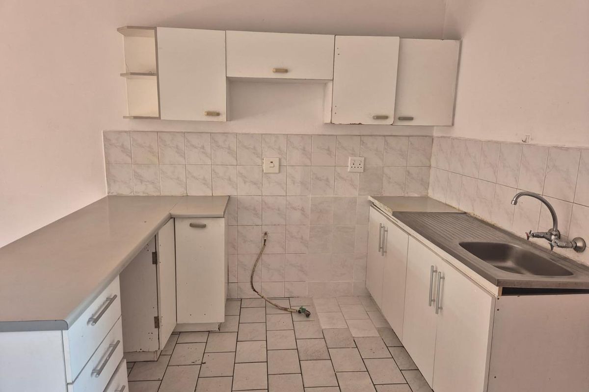 A dated kitchen featuring white cabinetry, laminate countertops, a stainless steel sink, and tiled flooring, offering a blank canvas for renovation.