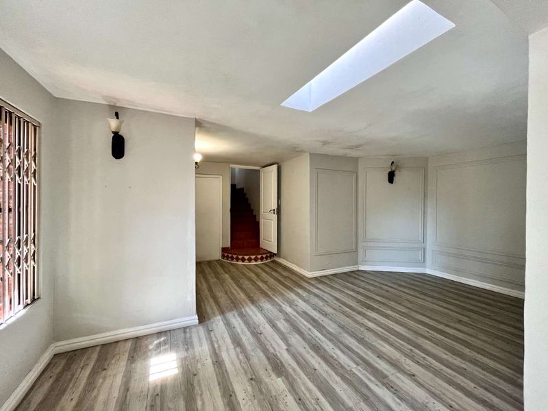 Spacious living area featuring laminate flooring, wainscoting, wall sconces, and a skylight, with a staircase leading to an upper level.