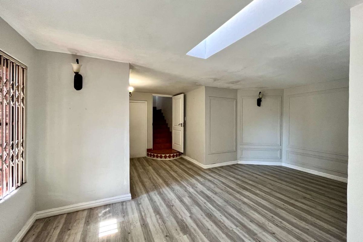 Spacious living area featuring laminate flooring, wainscoting, wall sconces, and a skylight, with a staircase leading to an upper level.