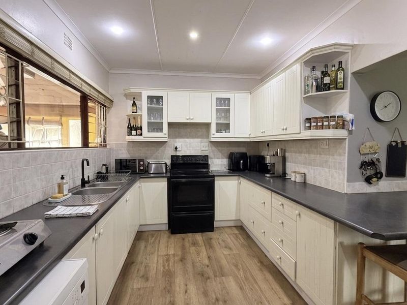 A well-maintained kitchen featuring white cabinetry, dark laminate countertops, a double basin sink, and a freestanding oven with a tiled backsplash.