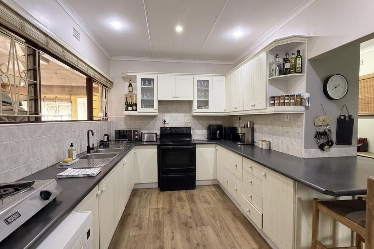 A well-maintained kitchen featuring white cabinetry, dark laminate countertops, a double basin sink, and a freestanding oven with a tiled backsplash.