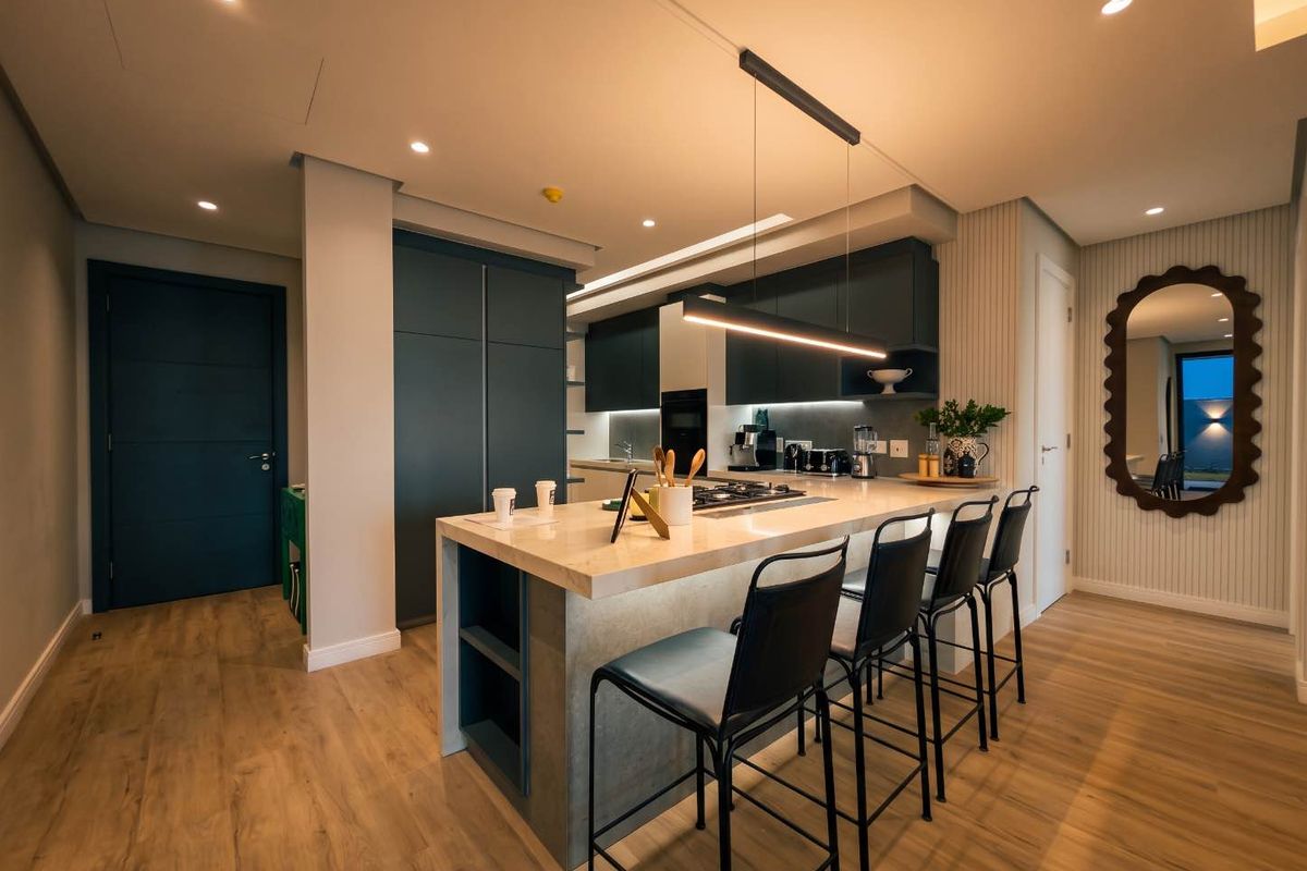 Modern kitchen featuring a central island with integrated cooktop, sleek dark cabinetry, recessed lighting, and high-quality laminate flooring in an open-plan layout.