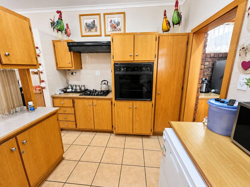 A functional kitchen featuring traditional wooden cabinetry, a built-in oven, gas hob, and tiled flooring, offering a classic layout with ample storage space.