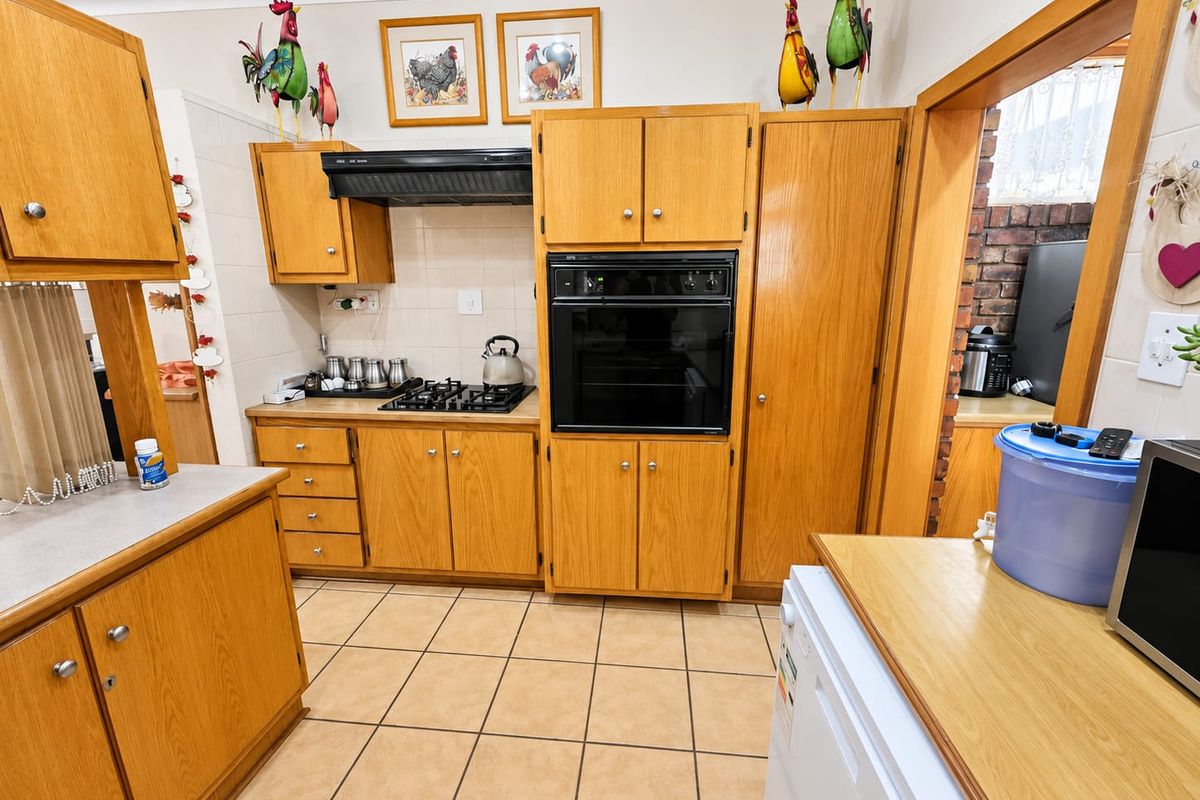 A functional kitchen featuring traditional wooden cabinetry, a built-in oven, gas hob, and tiled flooring, offering a classic layout with ample storage space.