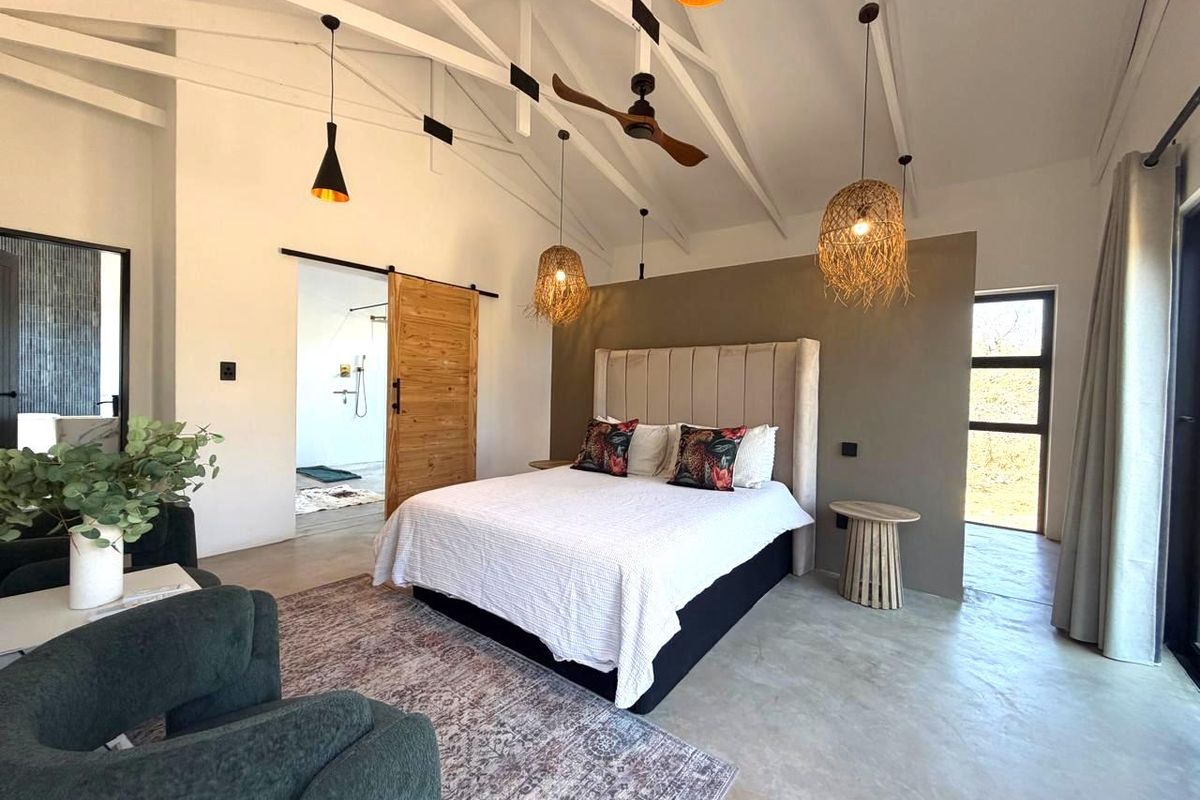 Spacious bedroom featuring high vaulted ceilings with exposed trusses, polished concrete floors, and a sliding barn door leading to an en-suite bathroom.