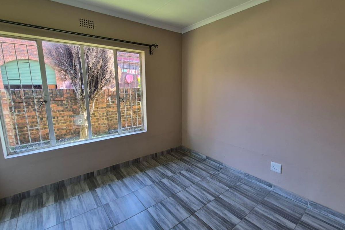 A bright, empty bedroom featuring tiled flooring, large windows with security bars, and neutral wall tones, offering a clean canvas for personalization.