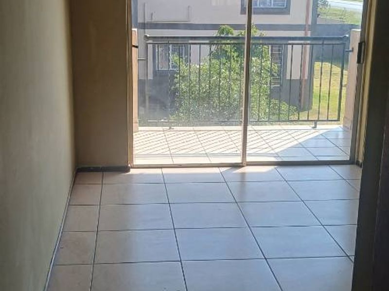 An empty living room featuring ceramic floor tiles and a large sliding glass door providing access to a balcony.