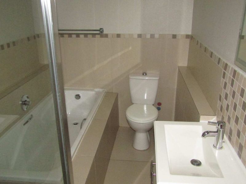 A clean, functional bathroom featuring a built-in bathtub, a modern vanity basin, and a toilet with neutral tiled finishes.