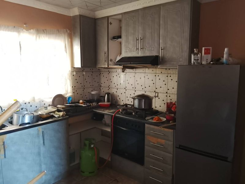 A functional kitchen featuring built-in cabinetry, a gas hob with extractor fan, and tiled backsplash, requiring some maintenance and cosmetic updates.