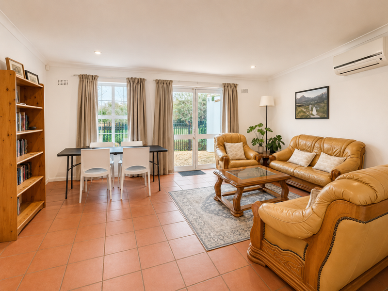 Spacious living area featuring terracotta floor tiles, a wall-mounted air conditioning unit, and direct access to the outdoor patio through double glass doors.