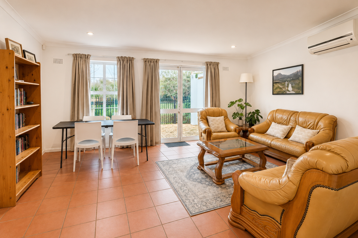Spacious living area featuring terracotta floor tiles, a wall-mounted air conditioning unit, and direct access to the outdoor patio through double glass doors.