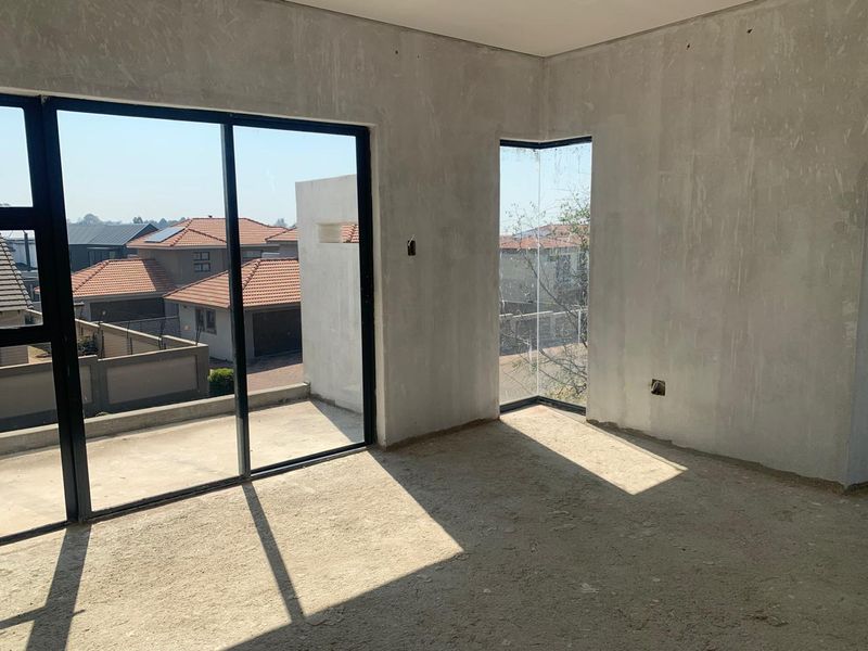 An unfinished bedroom interior featuring plastered walls, cement screed flooring, and large sliding glass doors leading to an outdoor area.