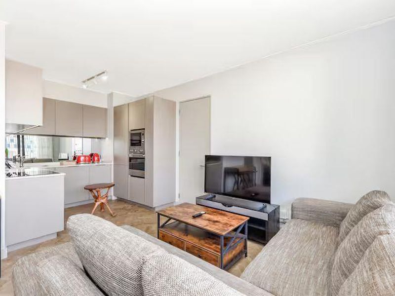 Modern open-plan living area featuring a sleek kitchen with integrated appliances, mirror splashback, and neutral finishes, seamlessly flowing into the lounge space.