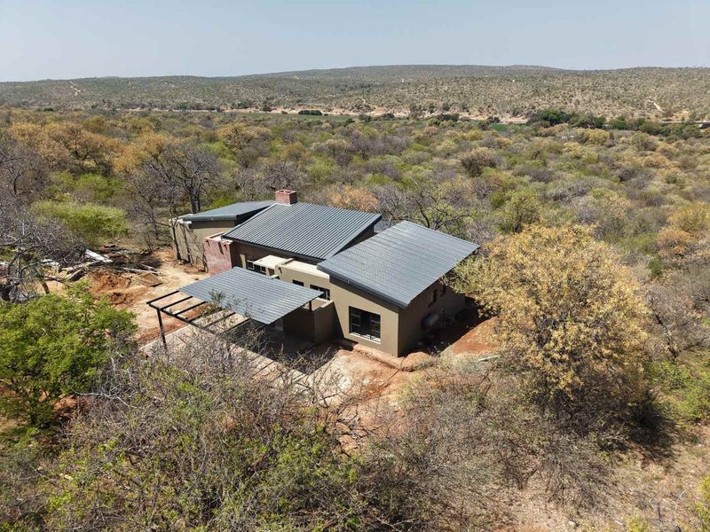 Aerial view of a modern house with a metal roof and covered patio, situated in a natural bushveld landscape.