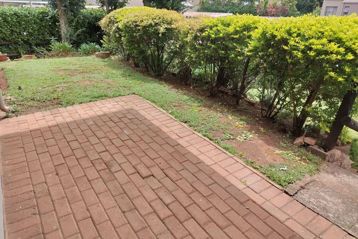 A rear garden area featuring a brick-paved patio space bordered by established hedges and a lawn area.