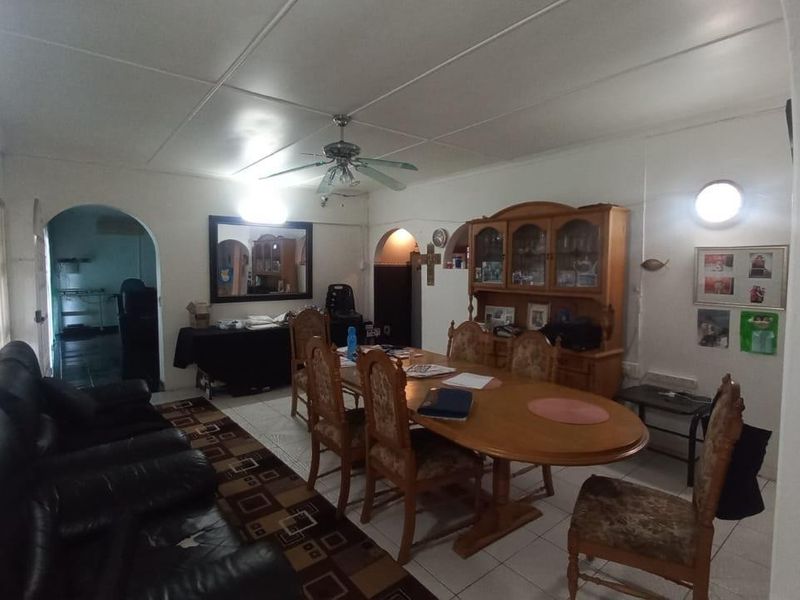 A dated living and dining area featuring tiled flooring, a ceiling fan, and arched doorways leading to adjacent rooms.
