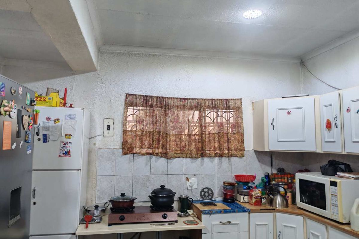 A functional kitchen featuring built-in cabinetry, a tiled backsplash, and security bars on the window, requiring some cosmetic updates to improve its overall condition.