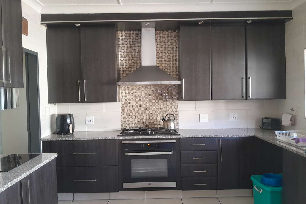 Modern kitchen featuring dark wood cabinetry, granite countertops, a mosaic tile backsplash, and integrated stainless steel appliances including an oven and gas hob.
