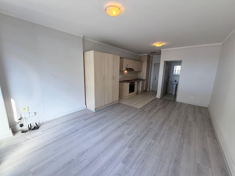 Open plan living area featuring laminate flooring, built-in kitchen cabinetry with integrated appliances, and direct access to an adjacent bathroom.