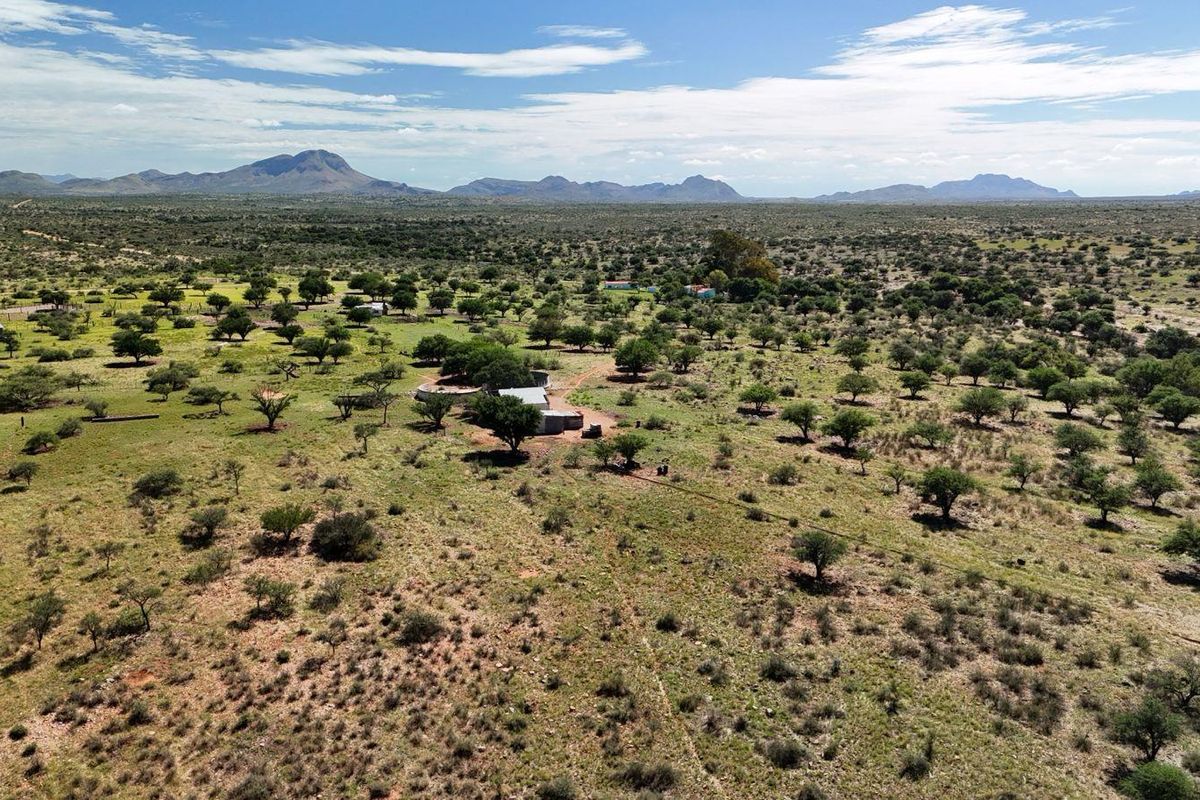 An aerial view of a vast farm property featuring open grazing land, scattered indigenous trees, and distant mountain vistas.