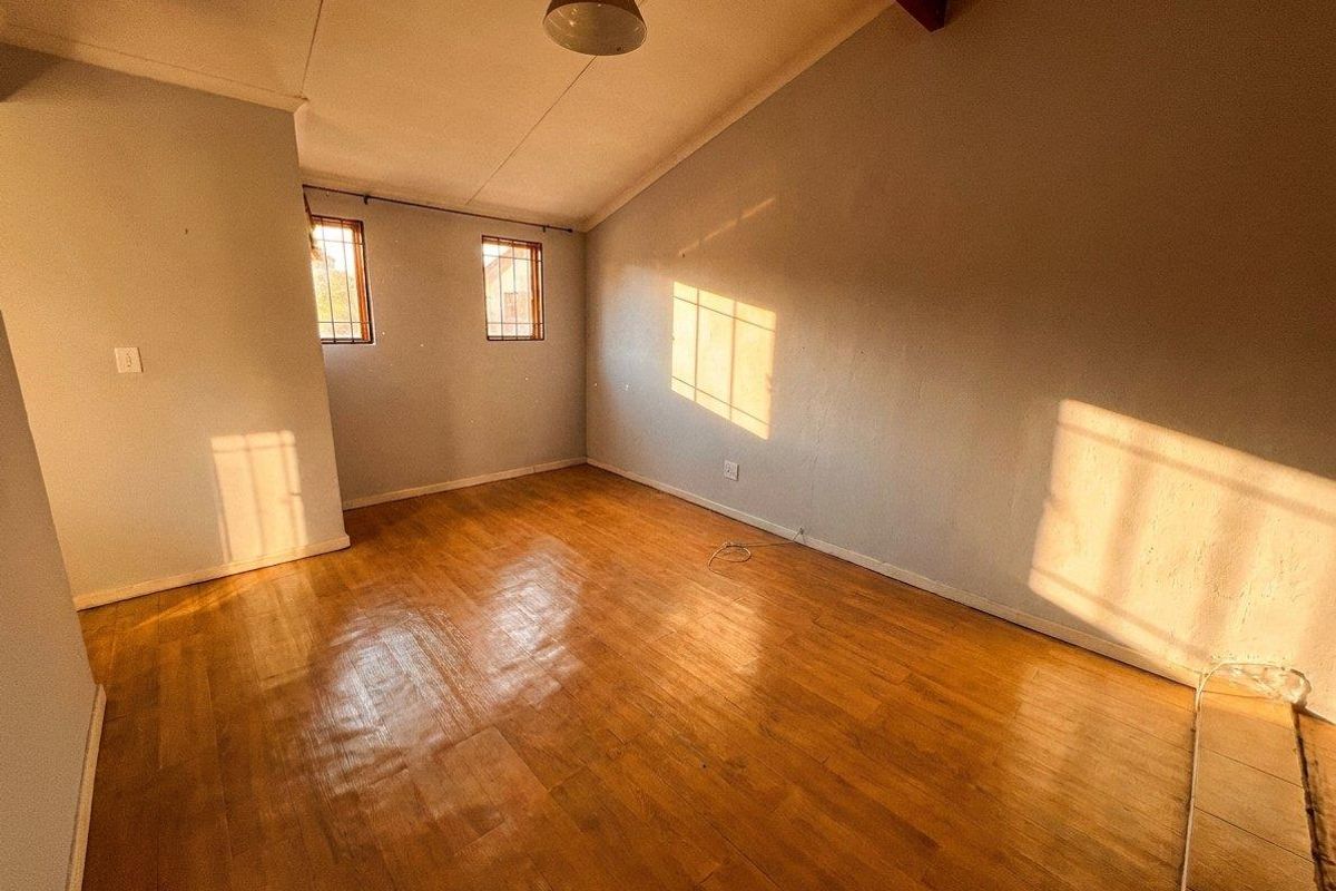 A vacant bedroom featuring vaulted ceilings with an exposed timber beam, laminate flooring, and security bars on the windows.