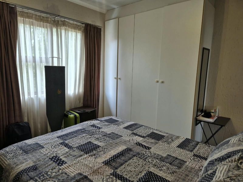 A bedroom featuring built-in cupboards and large windows with curtain rails, providing natural light and storage space.