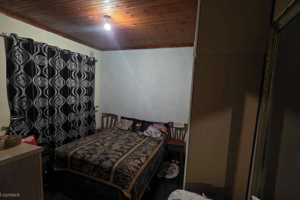 A bedroom featuring a timber ceiling, tiled flooring, and a built-in wardrobe, offering a functional space with potential for modern updates.