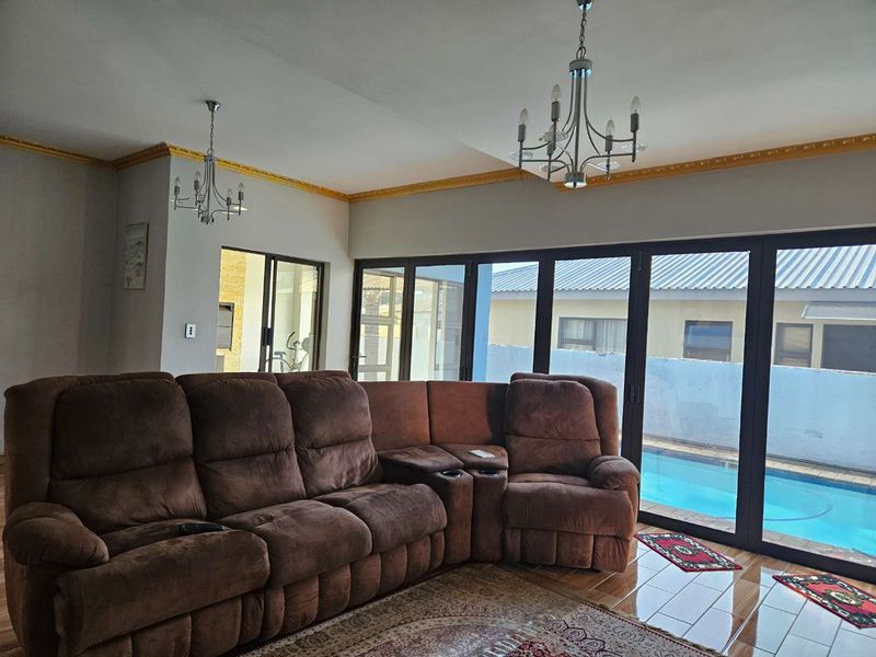 Spacious living room featuring large sliding glass doors with direct pool access, decorative gold crown molding, and dual chandeliers.