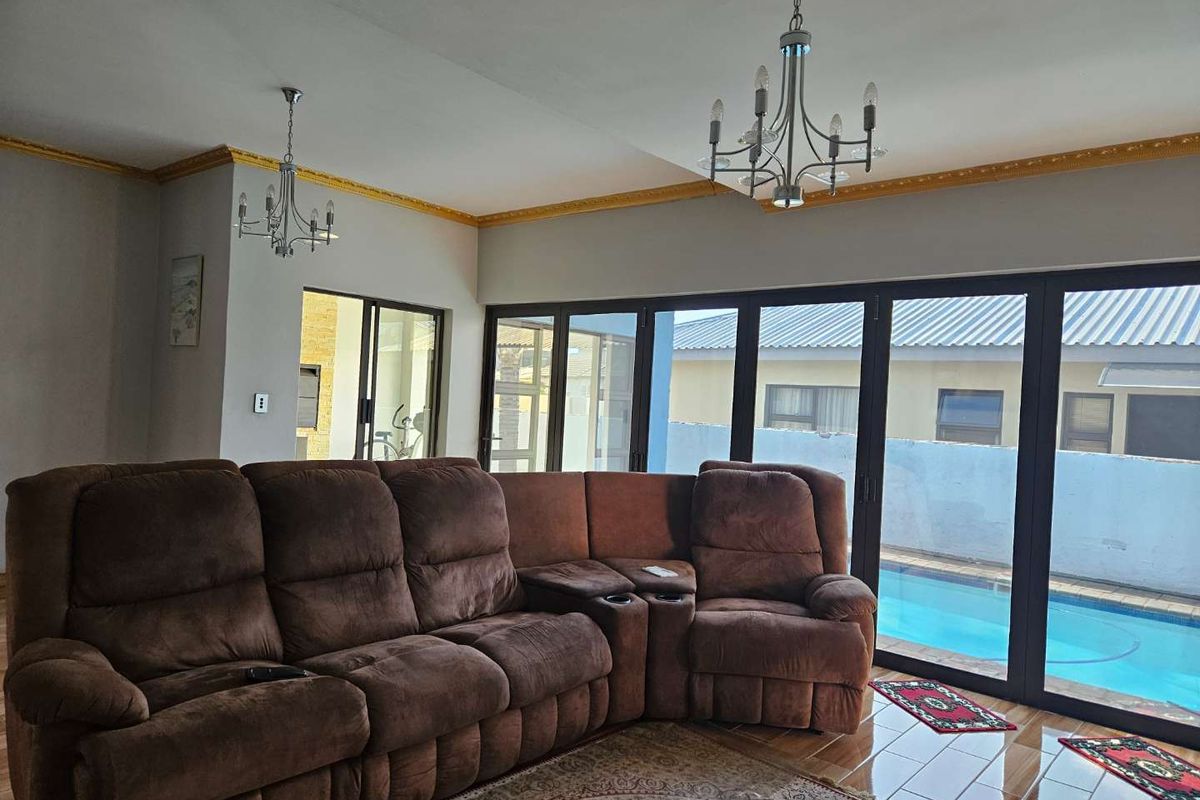 Spacious living room featuring large sliding glass doors with direct pool access, decorative gold crown molding, and dual chandeliers.