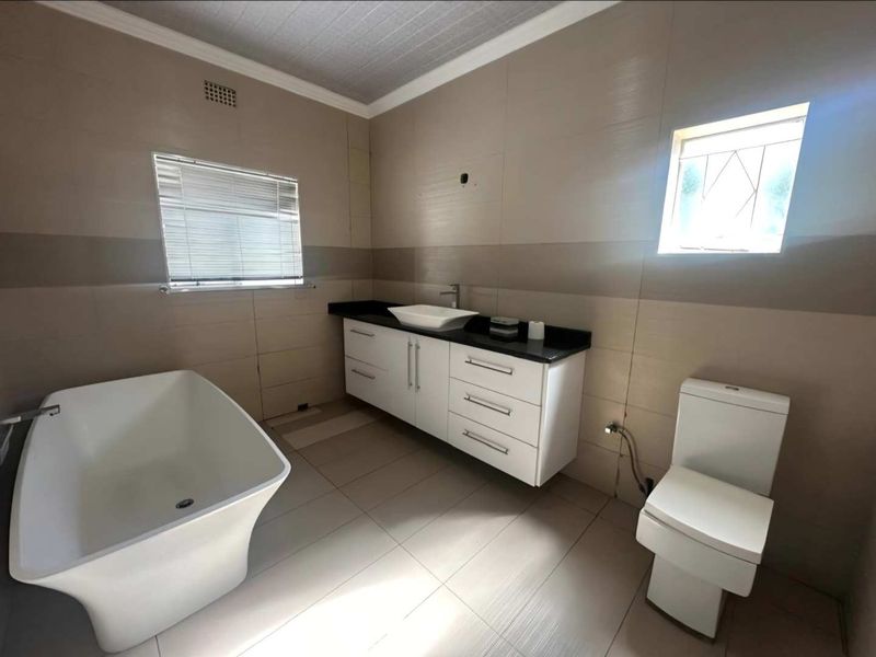 A modern, neutral-toned bathroom featuring a freestanding bathtub, a floating vanity with a vessel sink, and tiled finishes throughout.