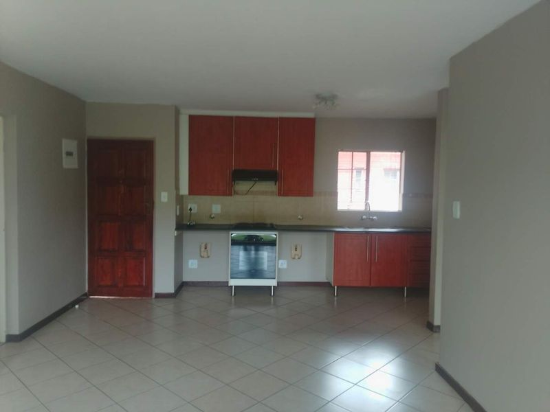 Open plan kitchen area featuring wooden cabinetry, a freestanding stove, and tiled flooring, offering a functional and clean space ready for personalization.