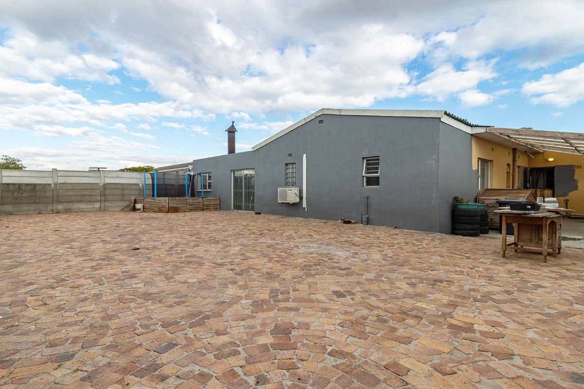 Spacious rear courtyard featuring extensive paving, a precast boundary wall, and a covered patio area, offering potential for outdoor entertainment and landscaping.