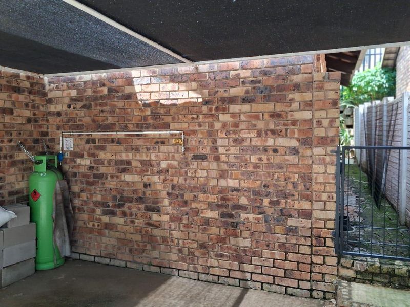 A covered outdoor patio area featuring exposed brick walls and direct access to a side garden path via a metal gate.