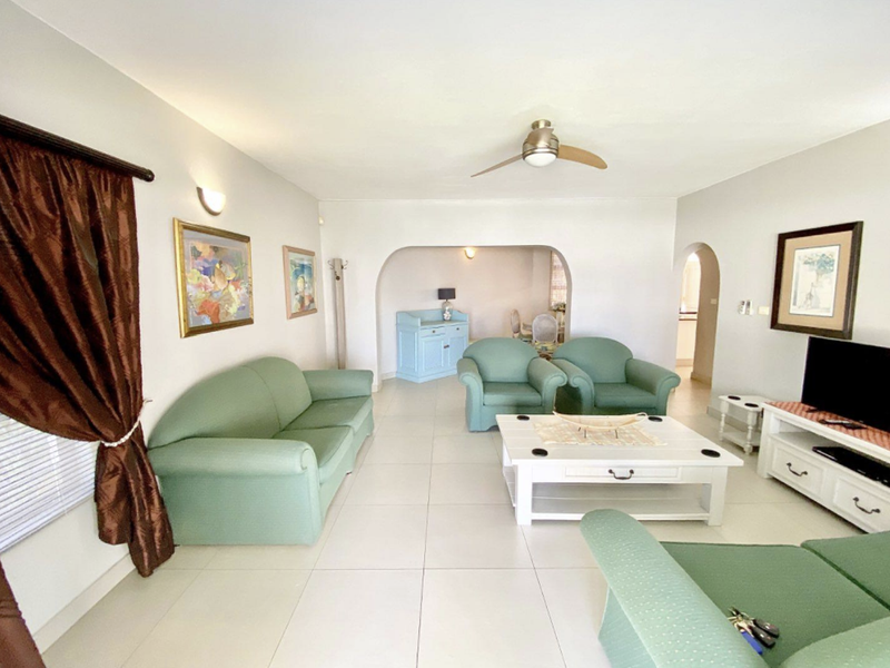 Spacious living room featuring neutral tiled flooring, a ceiling fan, and an arched entryway leading to an adjacent space.