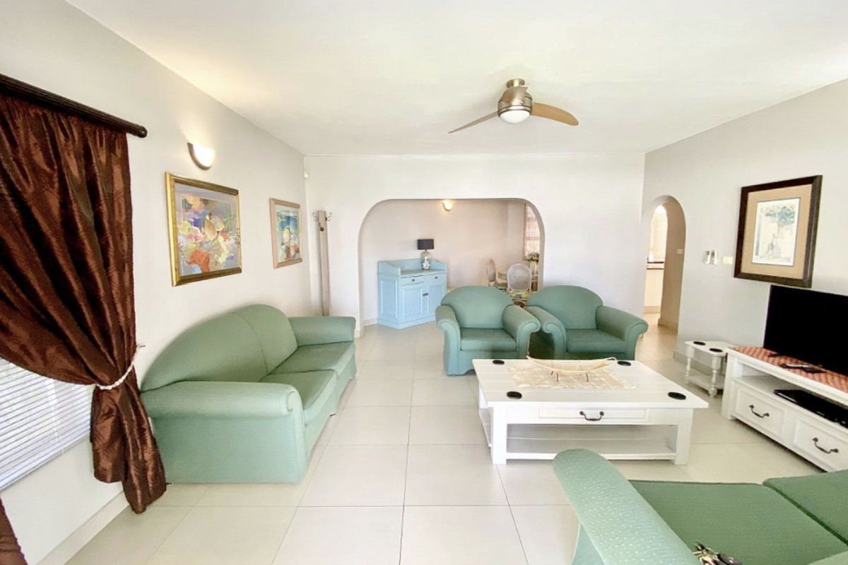 Spacious living room featuring neutral tiled flooring, a ceiling fan, and an arched entryway leading to an adjacent space.