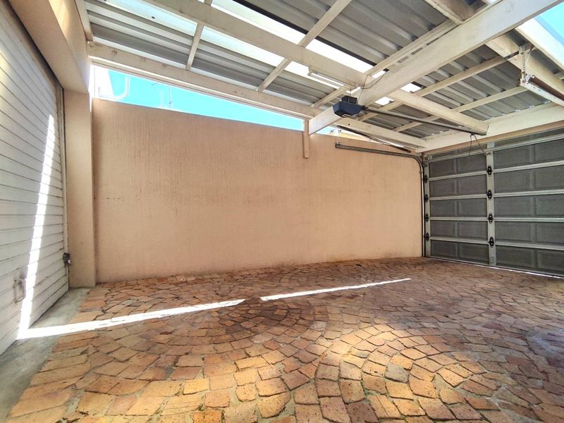 A spacious, empty garage featuring a sectional door, automatic motor, and durable cobblestone flooring under a corrugated metal roof structure.