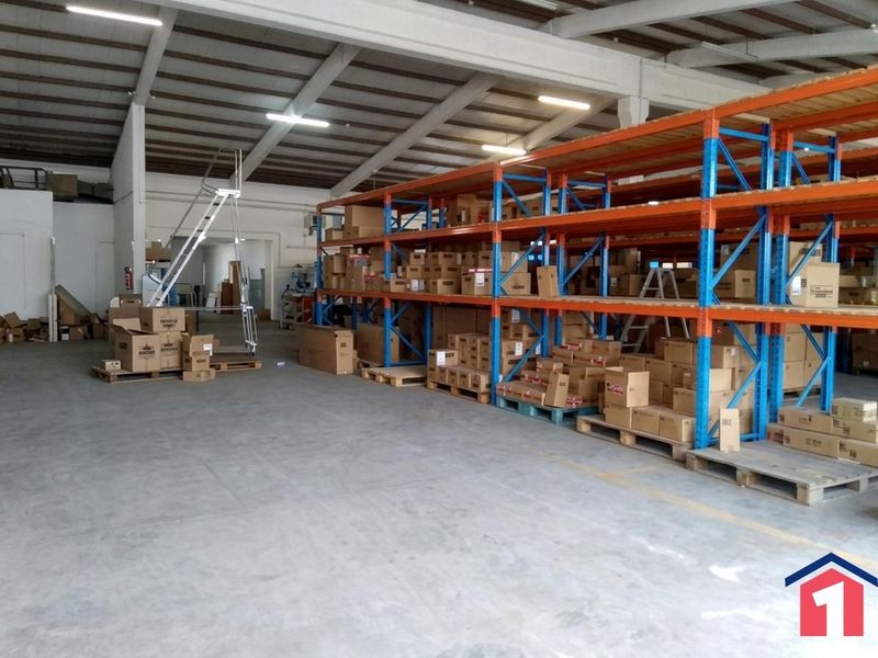 Spacious industrial warehouse featuring high ceilings with exposed steel trusses, concrete flooring, and extensive heavy-duty racking systems for storage.