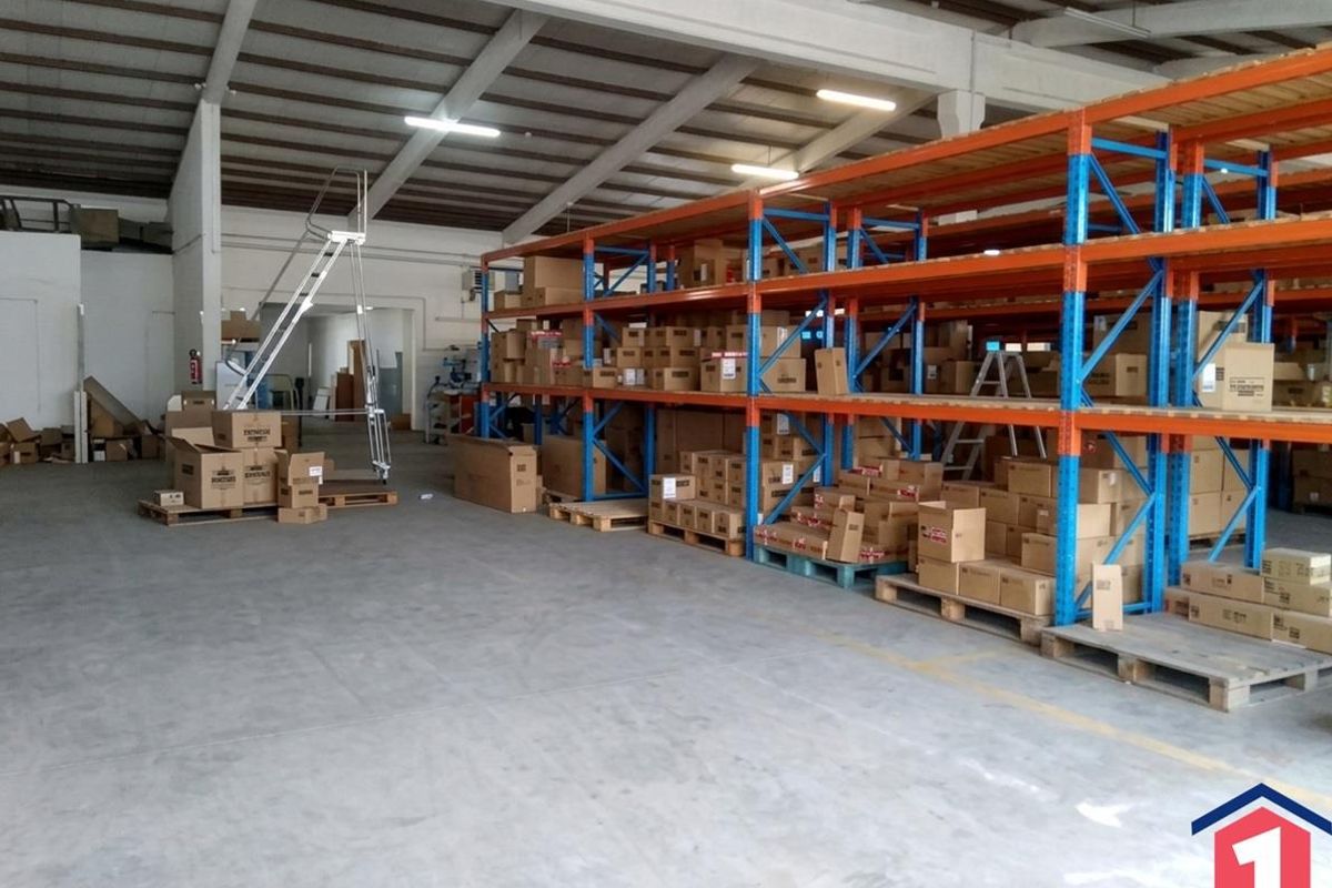 Spacious industrial warehouse featuring high ceilings with exposed steel trusses, concrete flooring, and extensive heavy-duty racking systems for storage.