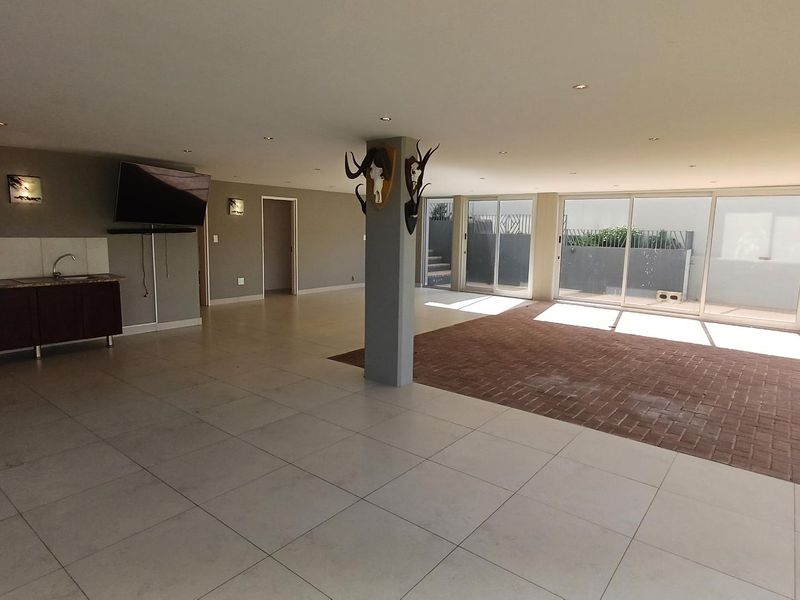 Spacious open-plan living area featuring tiled and brick flooring, a kitchenette, and large sliding glass doors providing ample natural light and outdoor access.