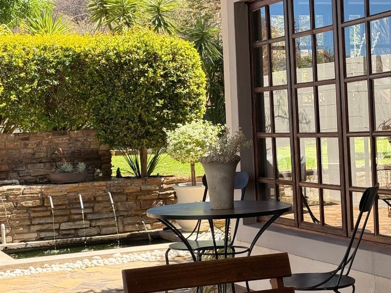 A covered patio area featuring tiled flooring, a timber ceiling, and a stone water feature, overlooking a landscaped garden.